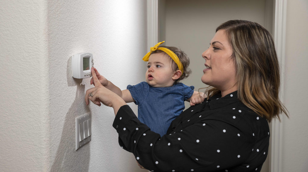 Mom with baby adjusting thermostat