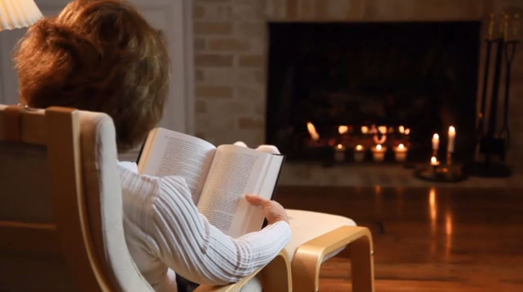 Woman reading a book by a fireplace.